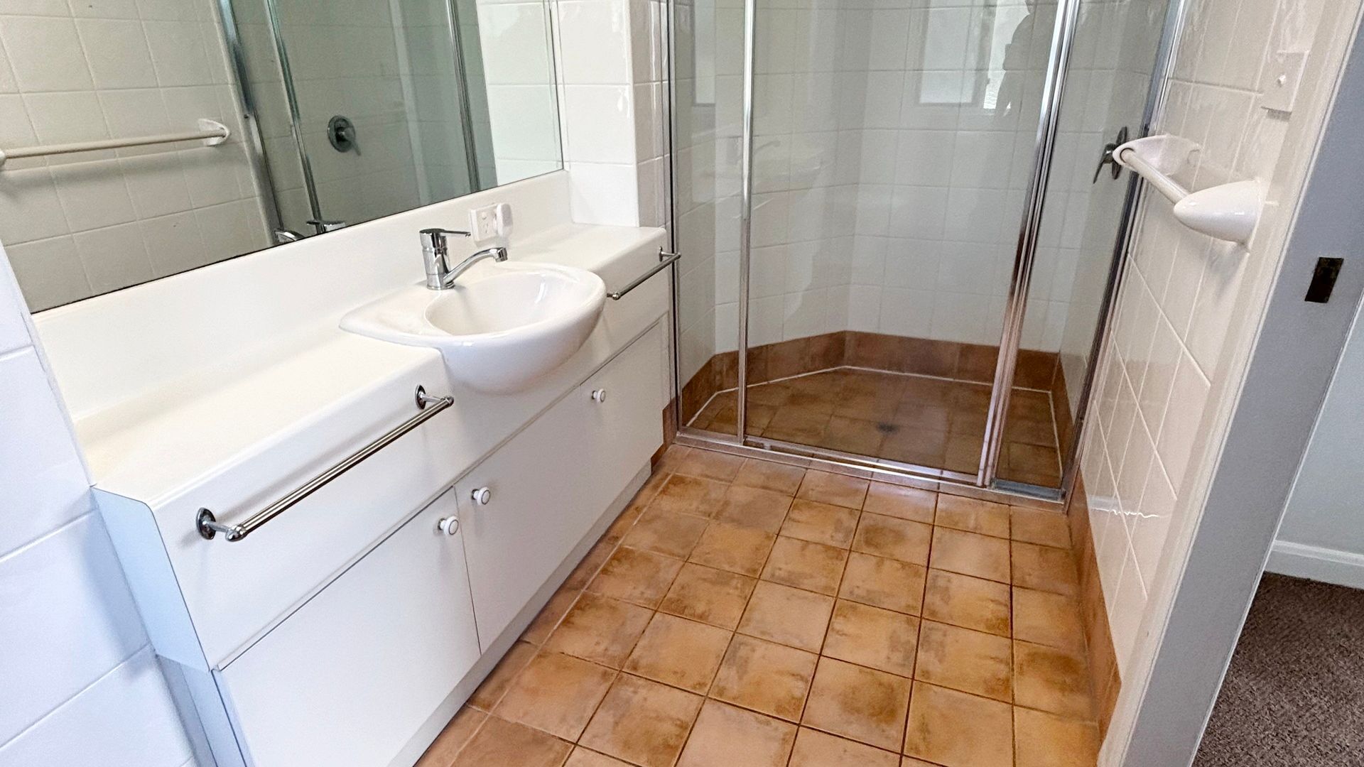 A bathroom with a white sink, mirror, and shower enclosure.