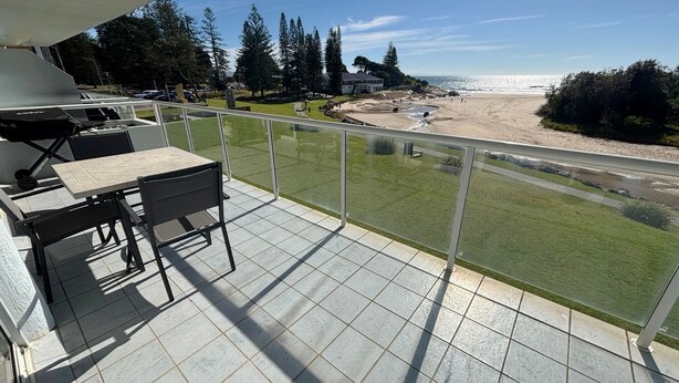 A balcony with a table and chairs, overlooking a beach and ocean. - Ocean Shores Apartment 15 - Bring your own linen (SOUTH WEST ROCKS)