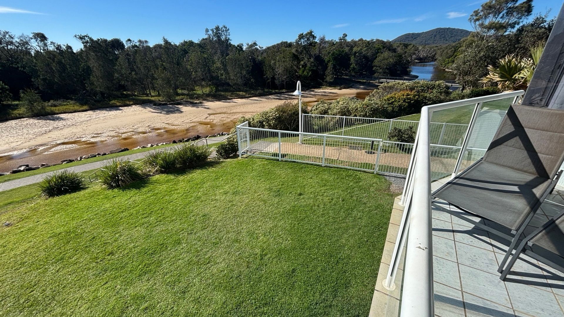 A balcony with a view of a river, a grassy area, and a metal railing.