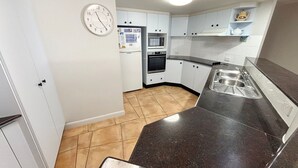 A kitchen with white cabinets, a microwave, oven, and a sink. - Ocean Shores Apartment 15 - Bring your own linen (SOUTH WEST ROCKS)