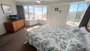 A bedroom with a bed, a dresser, a television, and large windows. - Ocean Shores Apartment 15 - Bring your own linen (SOUTH WEST ROCKS)
