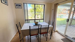A dining area with a table and chairs, a window with curtains, and a view of the outdoors. - Seldom Inn  - close to the water (SOUTH WEST ROCKS)
