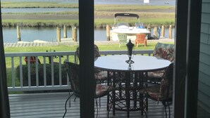 A deck with a table and chairs, overlooking a body of water with a boat and chairs docked nearby. - Fenwick Paradise Beach Villa-Beautiful Bayfront Condo .9Miles From The Beach<br> (Selbyville)