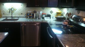 A kitchen with dark wooden cabinets, a stainless steel dishwasher, a coffee maker, and a stove. - Fenwick Paradise Beach Villa-Beautiful Bayfront Condo .9Miles From The Beach<br> (Selbyville)