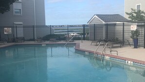 A swimming pool with a brick border, surrounded by a black fence, and adjacent to a building. - Fenwick Paradise Beach Villa-Beautiful Bayfront Condo .9Miles From The Beach<br> (Selbyville)