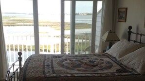 A bedroom with a large bed, a view of a body of water through a balcony, and a lamp on the nightstand. - Fenwick Paradise Beach Villa-Beautiful Bayfront Condo .9Miles From The Beach<br> (Selbyville)