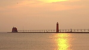 Escena costera con un faro y un muelle que se adentra en el agua al atardecer.