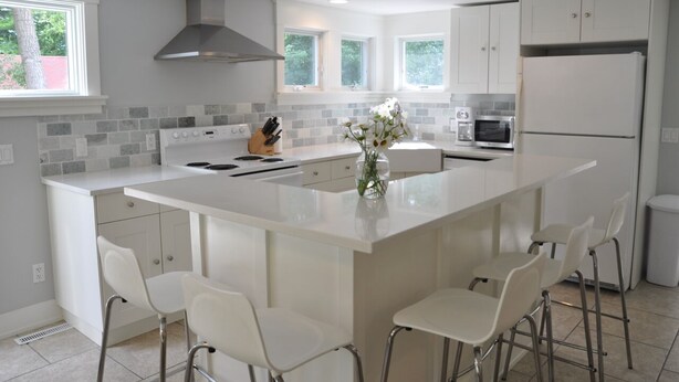 Una cocina moderna con una isla central, armarios blancos y una campana extractora de acero inoxidable.