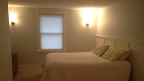 Un dormitorio con una cama individual, una ventana con persianas y dos lámparas fijadas a la pared.