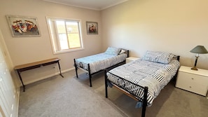 A bedroom with two single beds, a nightstand, a bench, and two wall-mounted paintings. - Parkview Lodge - walk to the beach (SOUTH WEST ROCKS)