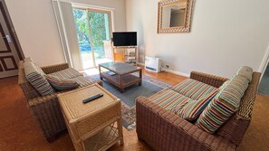 A furnished living room with wicker furniture, a television, and a large window. - Parkview Lodge - walk to the beach (SOUTH WEST ROCKS)