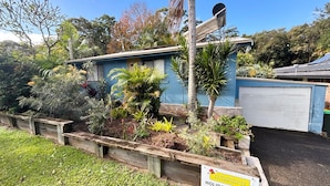 Un bâtiment bleu surmonté d’une antenne parabolique, entouré de différentes plantes et d’un panneau indiquant qu’il s’agit d’un logement de vacances.