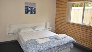 Una camera da letto con un letto singolo, biancheria bianca, una coperta decorata e un quadro di un ponte, con una parete in mattoni.