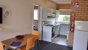 Una cucina compatta con elettrodomestici bianchi, un fornello e un lavello. Sul muro, un orologio e un estintore.