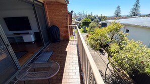 A balcony with a chair, a door leading to a garage, and a view of neighboring houses and trees. - Seacrest Unit 4 - walk to the beach (South West Rocks)