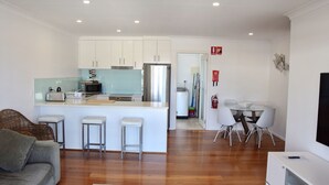 Eine moderne Küche mit weißen Schränken, einem Edelstahl-Kühlschrank und einer Kücheninsel aus Glas mit Barhocker.