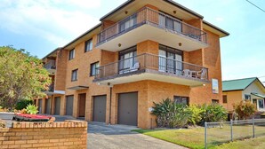 A multi-story brick building with balconies, a garage door, and a fenced yard. - Seacrest Unit 4 - walk to the beach - Bring your own linen (South West Rocks)