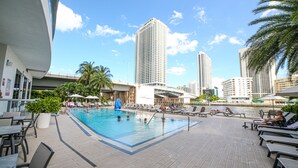 A rooftop pool with lounge chairs and palm trees, surrounded by tall buildings. - Private Ocean Luxury Condos at Beachwalk (Hallandale Beach)