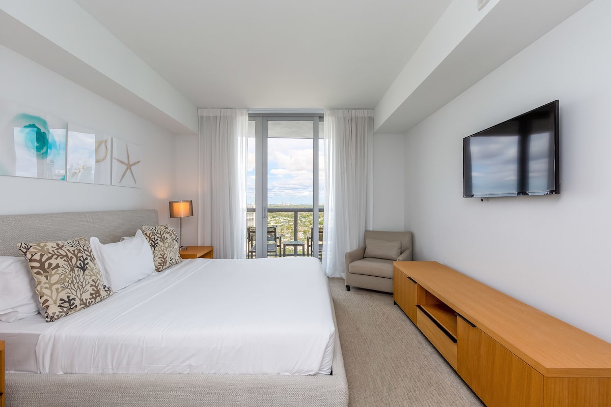 Une chambre d’hôtel avec un grand lit, un téléviseur fixé au mur, un canapé et un balcon avec vue.