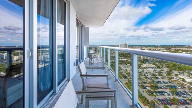 A balcony with a view of a parking lot and cityscape. - Private Ocean Luxury Condos at Beachwalk (Hallandale Beach)