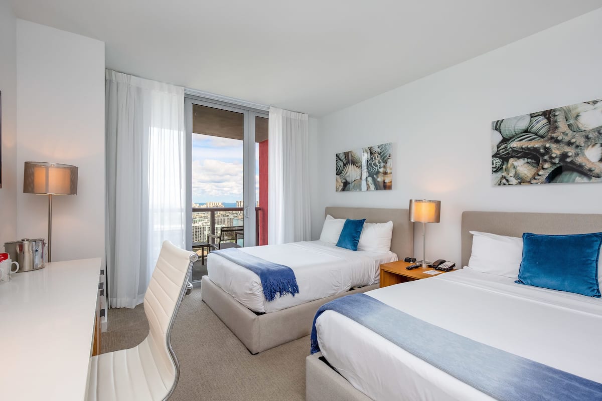 Une chambre d’hôtel avec deux lits, un bureau et une vue sur la ville.