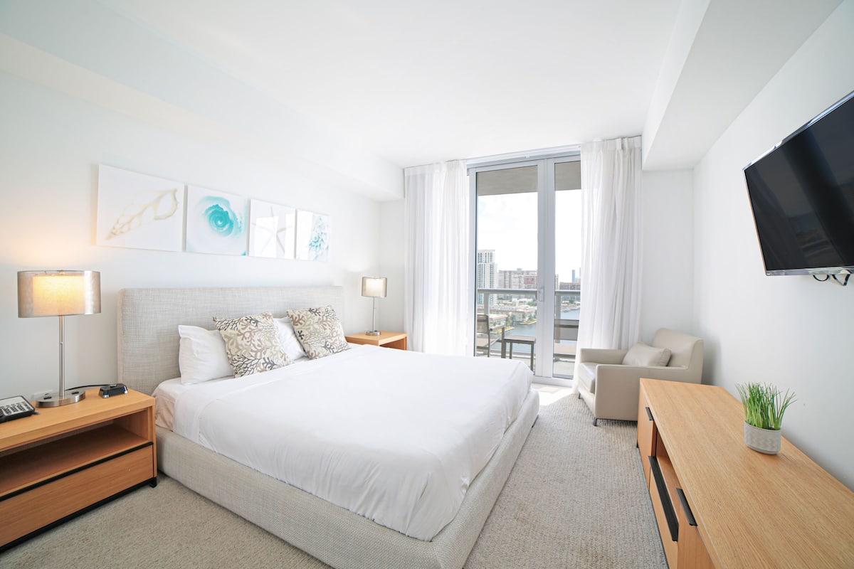Une chambre d’hôtel avec un grand lit, un bureau, une chaise, une télévision et des œuvres d’art accrochées au mur.