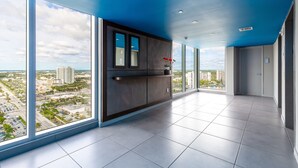 A spacious room with large windows, a dark wooden cabinet, and a view of a cityscape. - Private Ocean Luxury Condos at Beachwalk (Hallandale Beach)