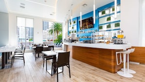 A modern restaurant with a bar area, wooden flooring, and a view of palm trees and buildings. - Private Ocean Luxury Condos at Beachwalk (Hallandale Beach)