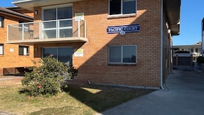 A two-story brick building with a sign reading 'PACIFIC COURT' and a balcony with a glass railing.