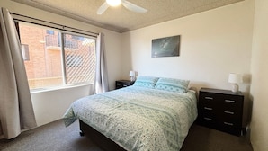 A bedroom with a bed, two bedside tables, a ceiling fan, a window with curtains, and a wall-mounted picture.