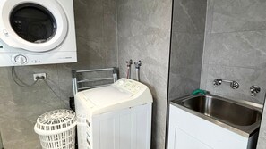 Un espace buanderie comprenant un lave-linge, un étendoir, un évier et un panier à linge.