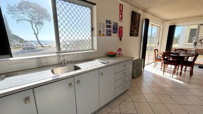 Une cuisine dotée d’une grande fenêtre, d’un évier, de placards et d’un coin repas avec des chaises et une table.