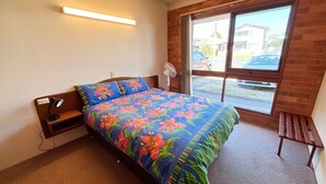Ein Schlafzimmer mit einem Bett, einem Nachttisch, einer Lampe, einem Fenster und Blick ins Freie.