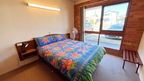 A bedroom with a bed, a bedside table, a lamp, a window, and a view of the outside.