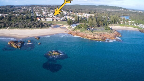 Luftaufnahme einer Küstenstadt mit Strand, Felsen und Wohnhäusern.
