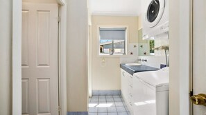 A narrow bathroom with a window, a sink, and a washing machine. - PJ's Cottage - walk to the beach (South West Rocks)