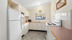 A compact kitchen with white appliances, a window, and a clock on the wall.
