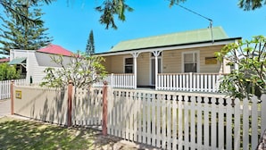 A two-story building with a green roof, a porch with white railings, and a sign indicating it is a holiday letting.