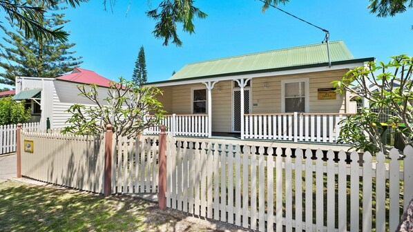 A two-story building with a green roof, a porch with white railings, and a sign indicating it is a holiday letting. - PJ's Cottage - walk to the beach (South West Rocks)