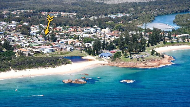 A coastal town with a beach, a bridge, and a marked area with a yellow arrow.