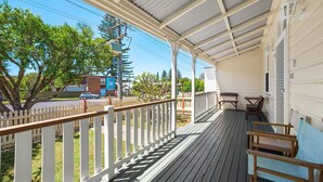A covered porch with a wooden deck, white railings, and a view of the street.