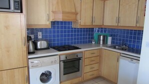 A compact kitchen with wooden cabinets, a washing machine, a microwave, a stove, and a dishwasher. - Sea View Apartment   situated on the seafront near the village Salthill (Galway)