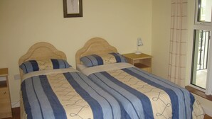 A double bed with striped bedding, a bedside table, a nightstand, a wall-mounted lamp, and a window with curtains. - Sea View Apartment   situated on the seafront near the village Salthill (Galway)