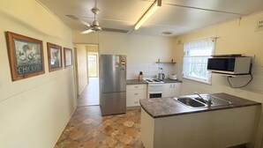 Eine kompakte Küche mit Kühlschrank, Herd, Mikrowelle und Spüle. An den Wänden hängen Bilder in Rahmen und es gibt einen Deckenventilator.
