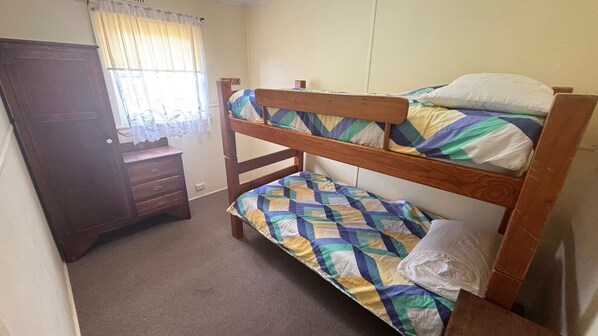 A bunk bed with a quilt, a wooden dresser, and a window with curtains.