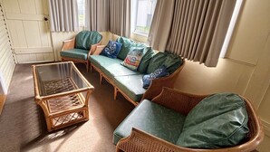 Ein gemütliches Zimmer mit einer Couch, einem Korbstuhl und einem Tisch mit Glasplatte.
