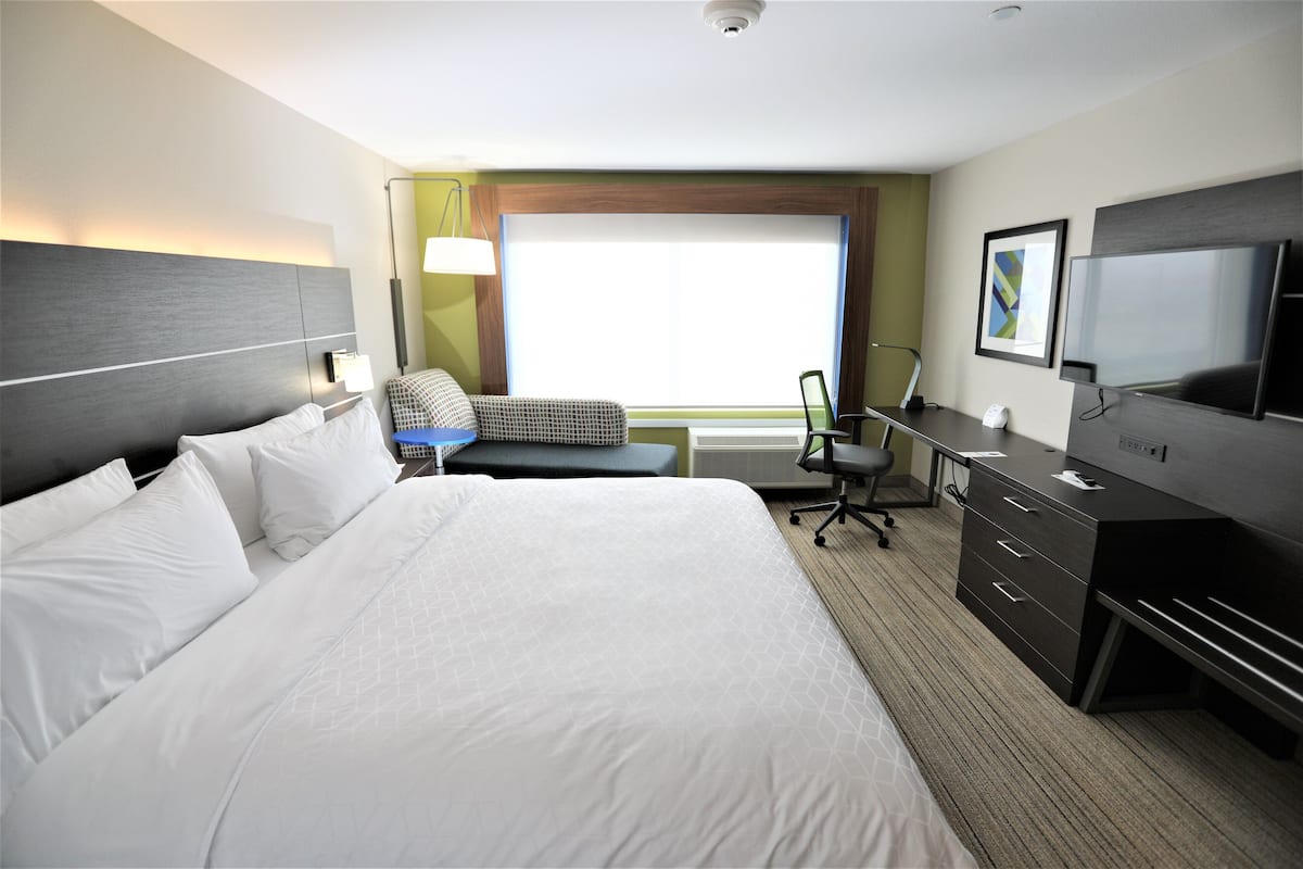 A hotel room with a large bed, a desk with a computer, a chair, and a TV.