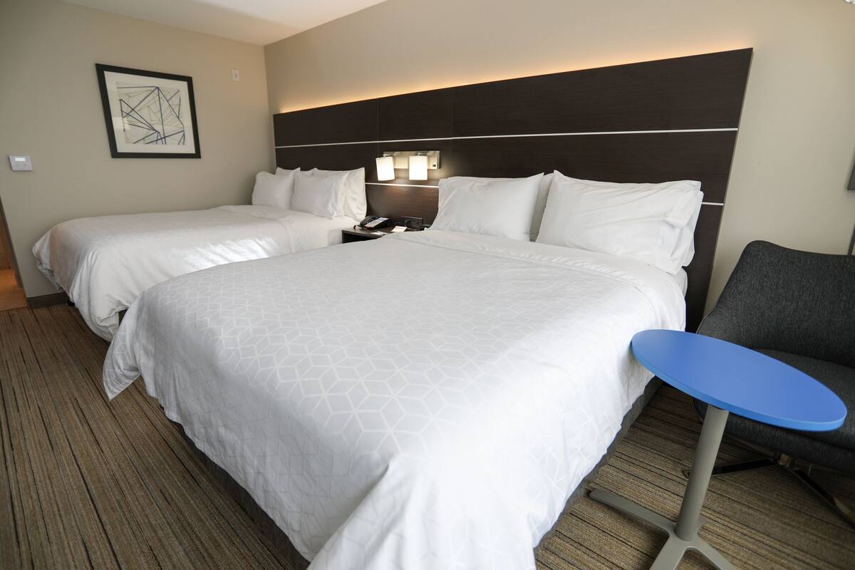 A hotel room with two beds, a nightstand, a desk, and a chair.