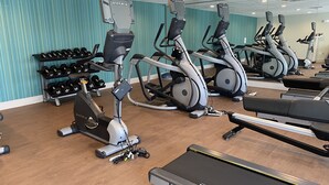 Une salle de sport équipée de plusieurs tapis de course, de plusieurs appareils elliptiques et d’une variété d’haltères.