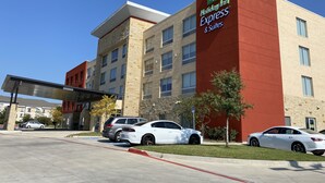 Un bâtiment de la chaîne Holiday Inn Express & Suites, doté d’un design moderne, avec une façade rouge et beige, de nombreuses fenêtres et un parking où sont stationnées plusieurs voitures.